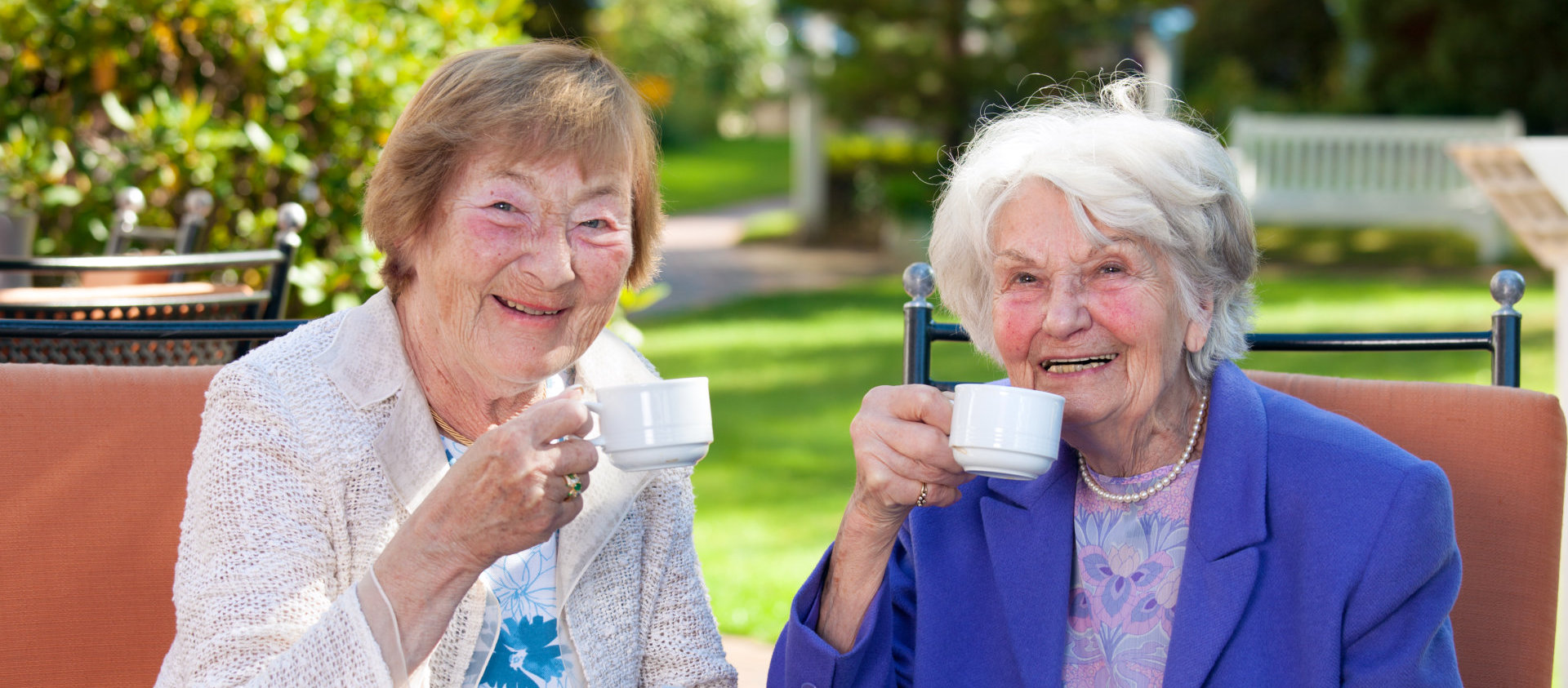 two senior woman holing a cup and smiling